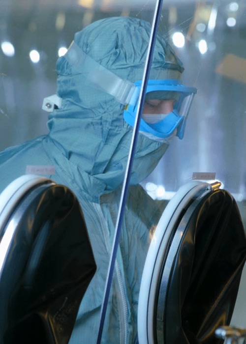 Gowned worker performing a procedure in the manufacturing of a highly potent compound