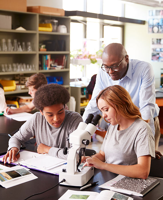 An employee works with two students using a microscope in a science study session